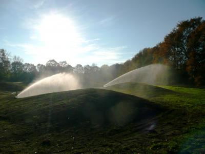 Sportplatzbewässerung im Einsatz mit Wasserstrahlen, die den Rasen auf einem weitläufigen Sportplatz gleichmäßig bewässern